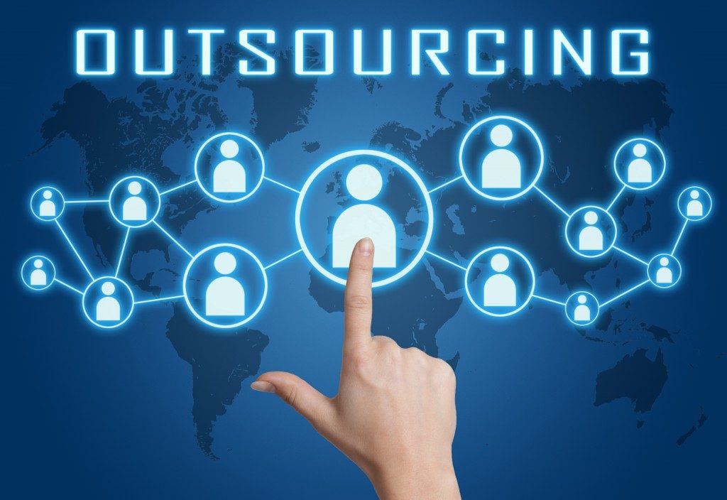 Outsourcing concept with hand pressing social icons on blue world map background.
